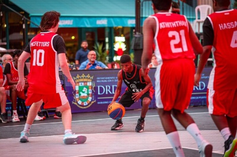 A player dribbles a ball on the court as onlookers watch, and his opponents surround him