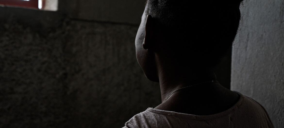 A 15-year-old girl, Taïna, stands in silhouette, looking out a window, symbolizing her resilience after surviving gender-based violence in Haiti and receiving support from UNICEF partner OFAVA.