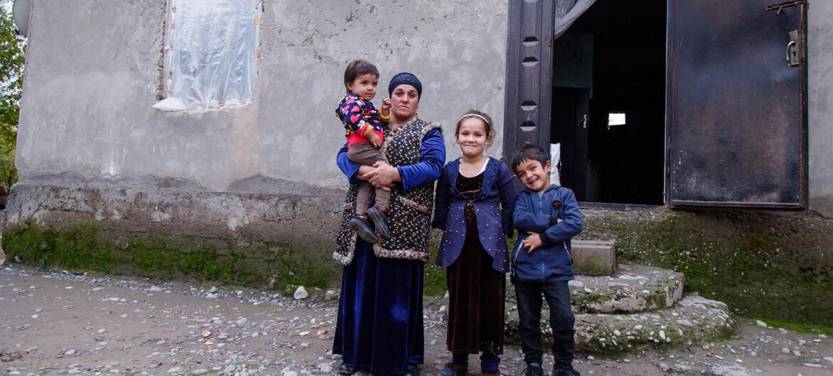 Shermatova Marjona, a 35-year-old mother of three in Tajikistan, stands with her children outside their home, highlighting the issue of gender-based violence and the need for social and legal support.