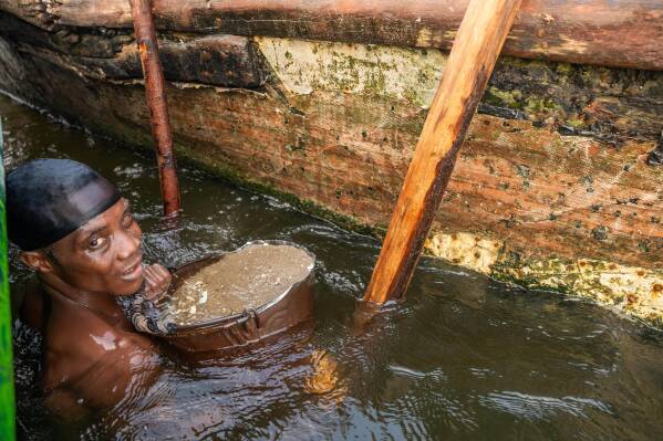One of thousands of local dredgers diving for sand to support his household on Saturday, Dec. 13, 2025. He said he and his partner earn about 12,000 naira ($8) each per boatload, selling to a middleman who supplies larger buyers. (AP Photo/Grace Ekpu)