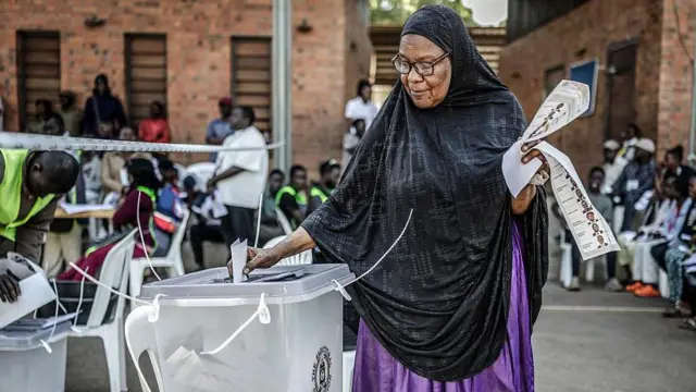 Voter in black headscarf place her vote for ballot box.