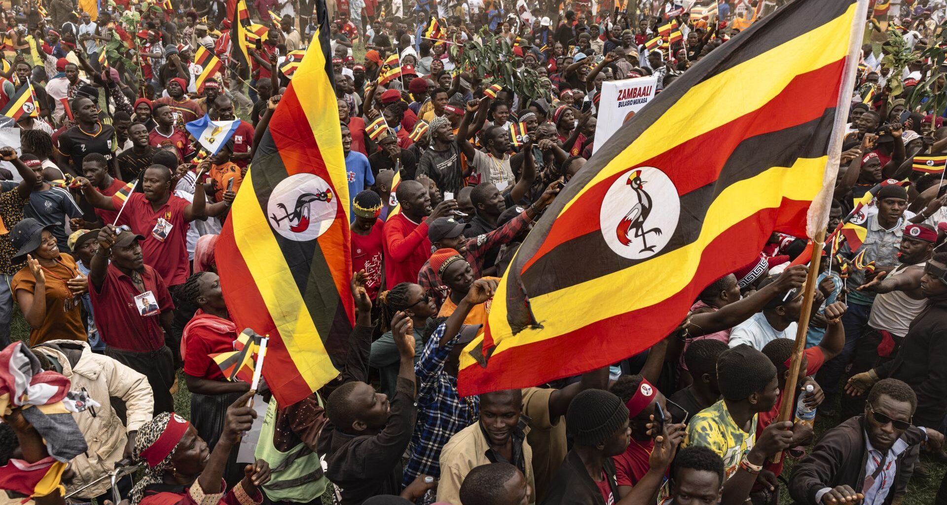 Supporters hold Ugandan flags as others cheer the arrival of Bobi Wine at the National Unity Platform's final campaign rally ahead of Uganda's 2026 general elections on January 13, 2026 in Kampala, Uganda.