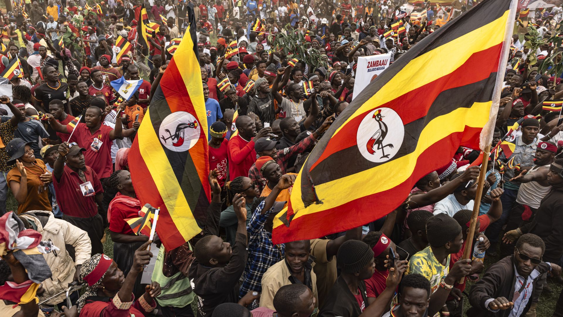 Supporters hold Ugandan flags as others cheer the arrival of Bobi Wine at the National Unity Platform's final campaign rally ahead of Uganda's 2026 general elections on January 13, 2026 in Kampala, Uganda.