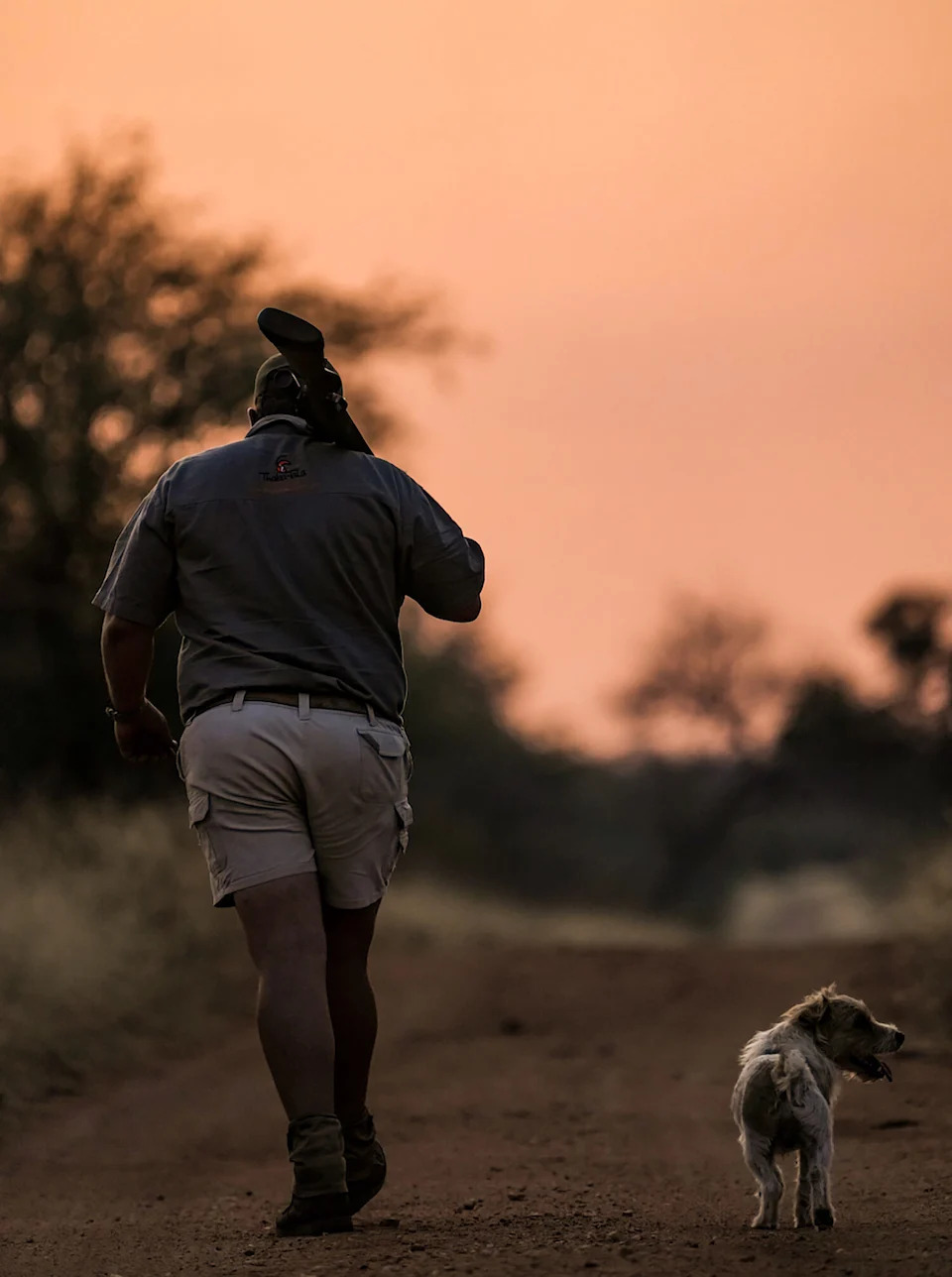 hunter and dog walk down dirt road as sunset creates rosy sky