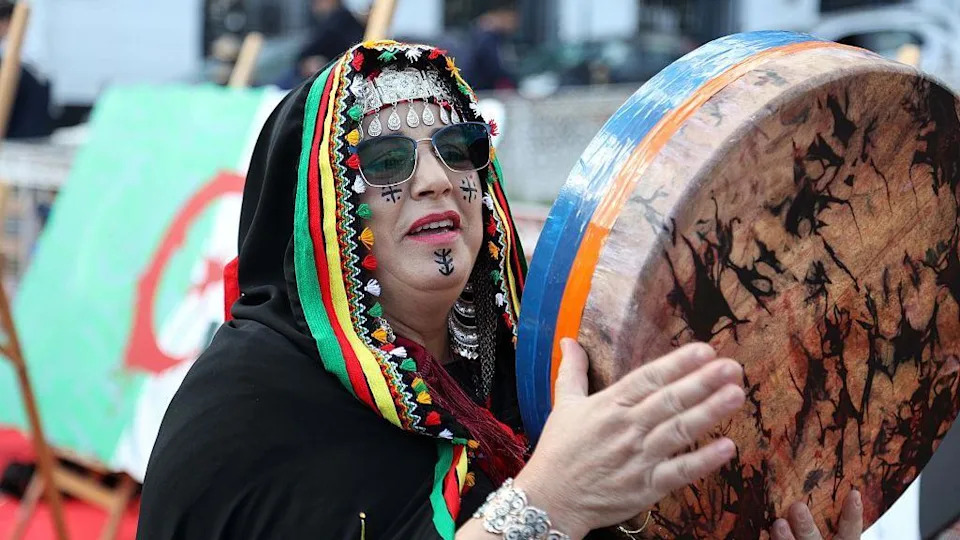 A women with a black, multi-coloured headscarf plays a percussive instrument