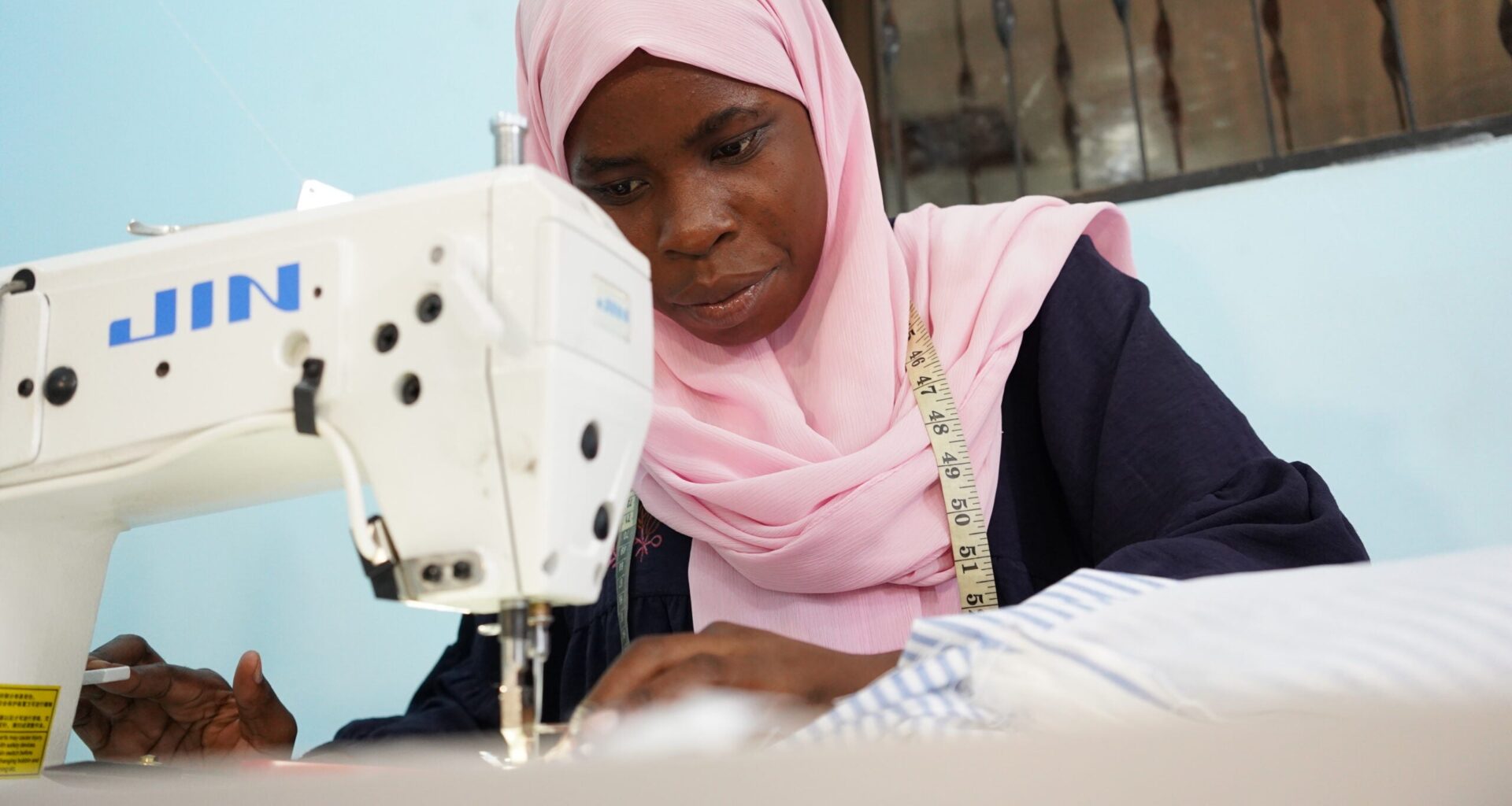A woman in a pink headscarf leans over a sewing machine at the Arizona Vocational Center in Dar es Salaam, Tanzania.