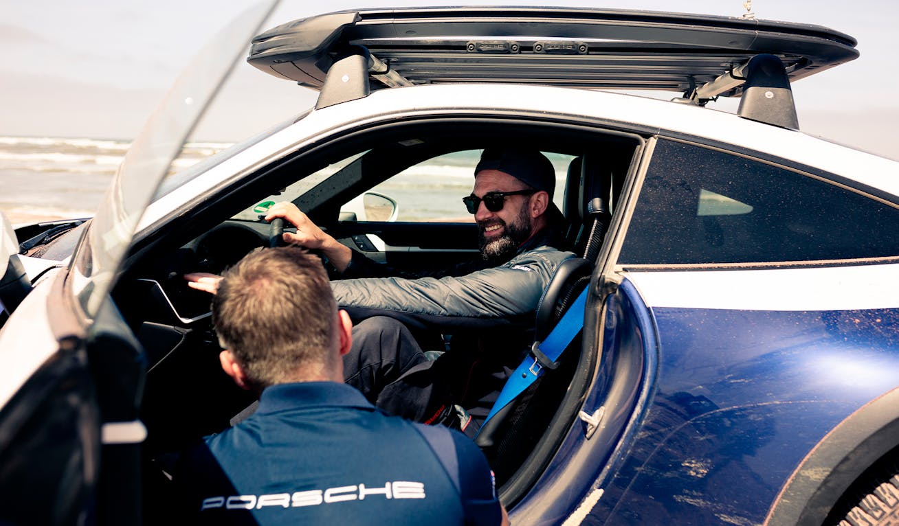 Man in Porsche 911 Dakar talking to man sitting outside