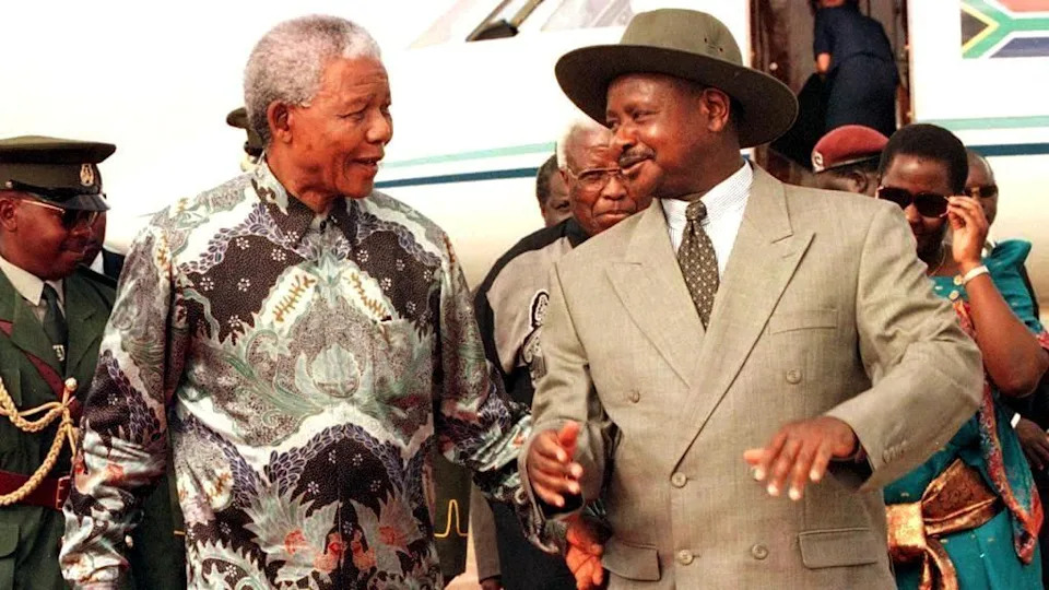 An old photo of Nelson Mandela talking to Yoweri Museveni, who wears one of his signature wide-brimmed hats and a suit