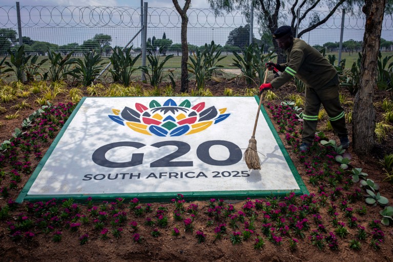 A worker sweeps a painted sign for the G20 Summit in South Africa that is sitting in a flower bed.