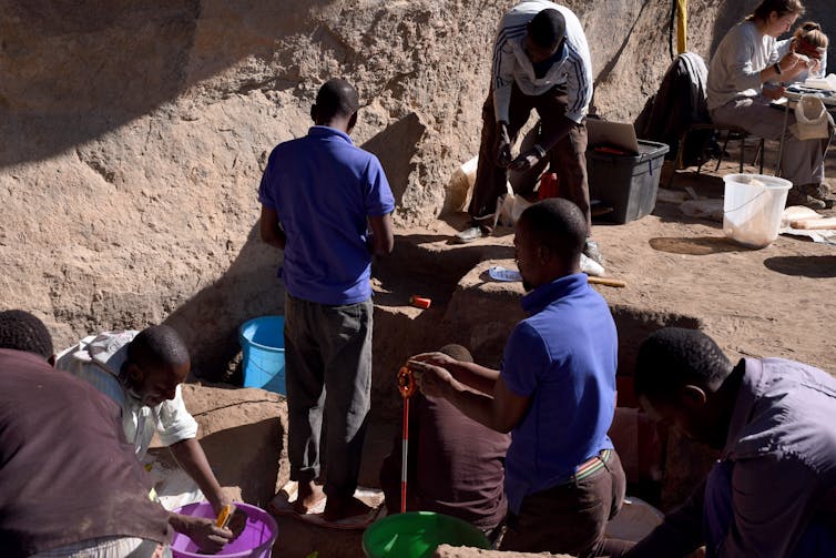 people with digging tools against a landscape that looks like hardpacked earth