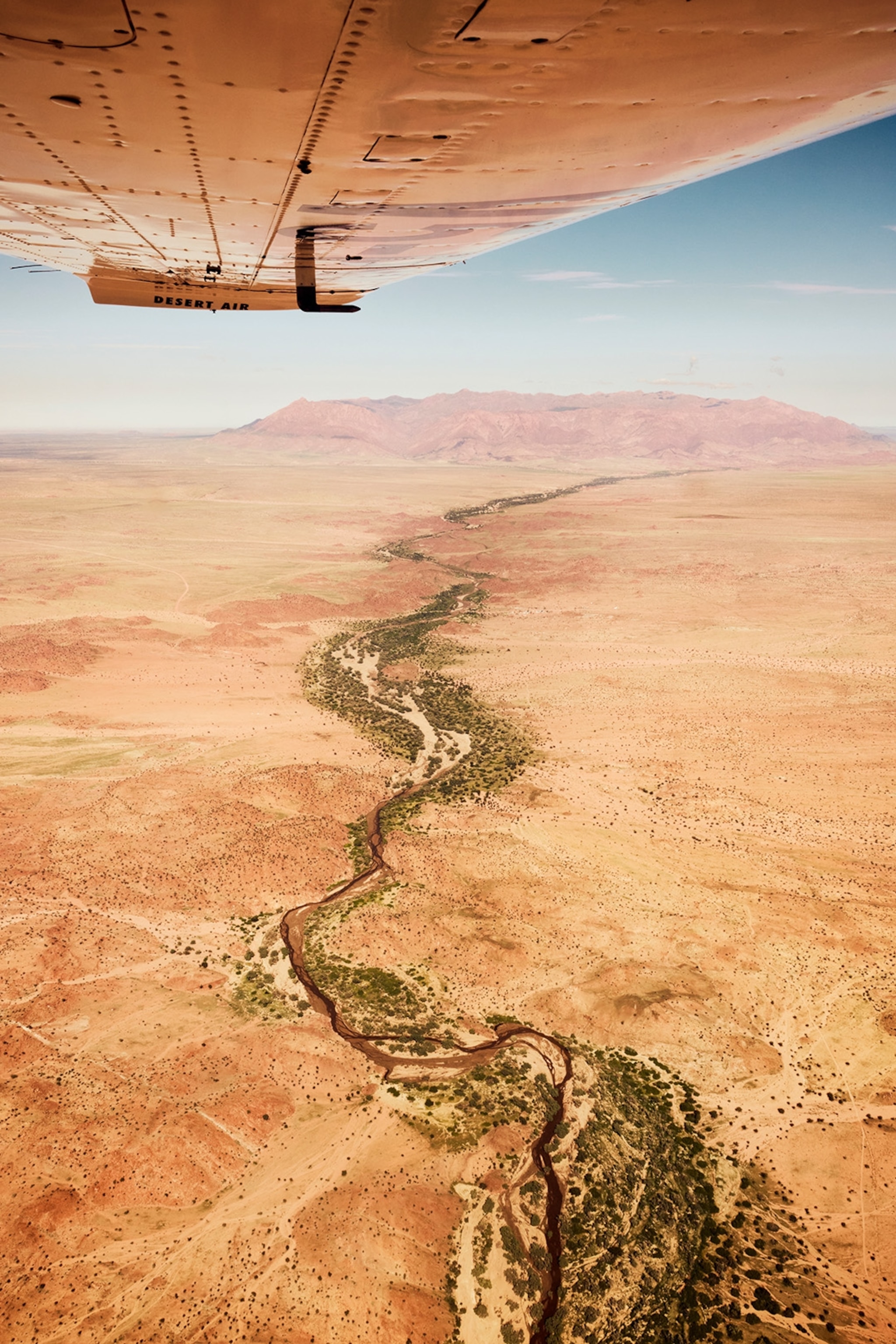 A small river lined with shrubbery winds through the desert.