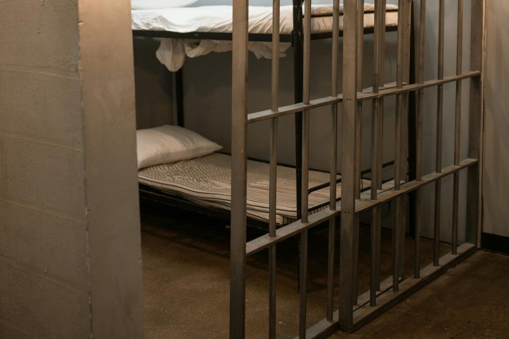 a bunk bed with striped linen behind bars prison cell