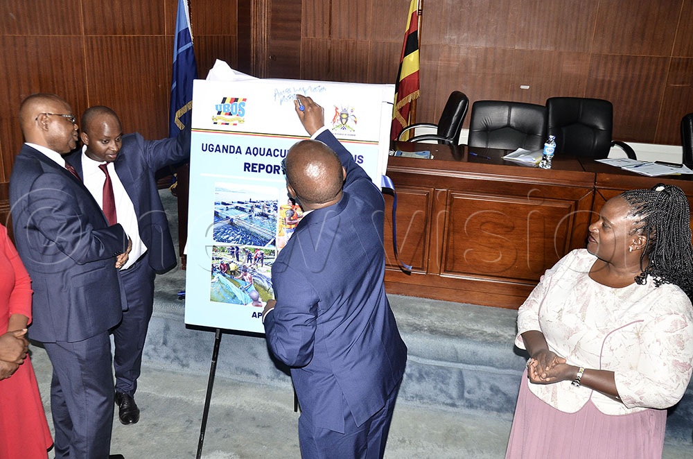 The Executive Director of the Uganda Bureau of Statistics (UBOS), Dr Chris N. Mukiza (L) looks on as the Minister of State for Finance, Planning, and Economic Development Amos Lugolobi, (C) signs on the board during the launch of first Uganda Aquaculture Census 2025 Report at UBOS offices in Kampala on April 30, 2026. Right is acting board chairperson, Rosette Nakavuma. (Credit: Ronnie Kijjambu)