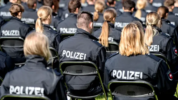 Polizistinnen und Polizisten des Bachelorstudienjahrgangs der Polizeiakademie Niedersachsen sitzen bei ihrer Abschlussfeier auf einem Sportplatz. | picture alliance/dpa/Hauke-Christian Dittrich, Hauke-Christian Dittrich Polizistinnen und Polizisten des Bachelorstudienjahrgangs der Polizeiakademie Niedersachsen sitzen bei ihrer Abschlussfeier auf einem Sportplatz.