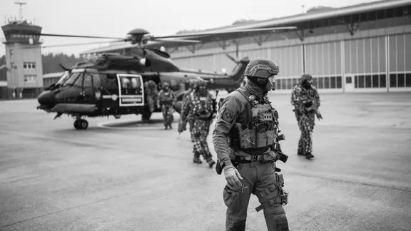 Einsatzkräfte einer Spezialeinheit gehen vor einem stehenden Hubschrauber entlang. | LKA Schleswig-Holstein Einsatzkräfte einer Spezialeinheit gehen vor einem stehenden Hubschrauber entlang.