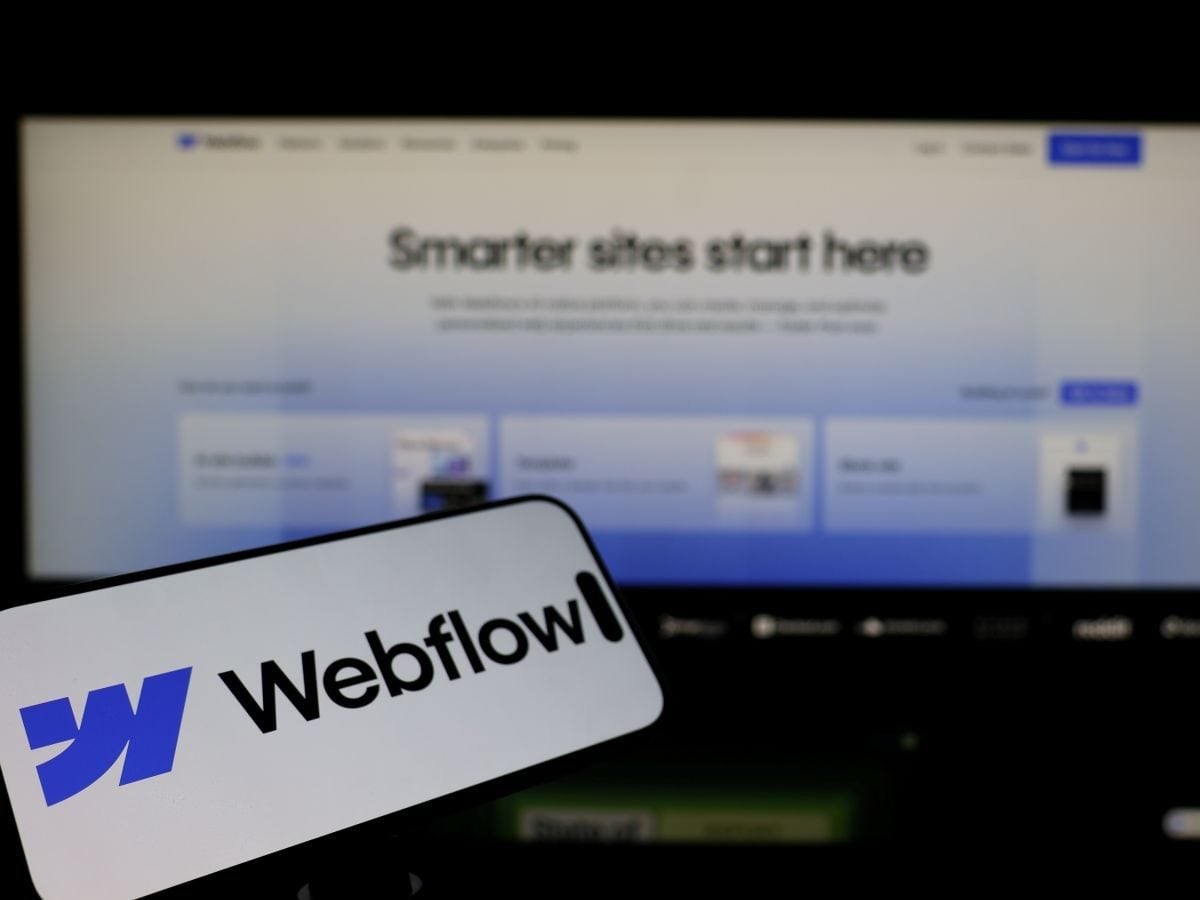 A blurred Webflow website homepage displayed on a screen with a Webflow logo sticker in the foreground.