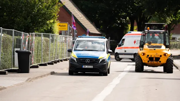 Nach Angaben des Veranstalters sind täglich rund 800 Polizisten, Feuerwehrleute, Sanitäter und Notärzte im Einsatz. | NDR / Dominik Dührsen Ein Polizei-Auto, ein Wagen vom Deutschen Roten Kreuz und ein gelber Gabelstabler fahren durch Wacken.