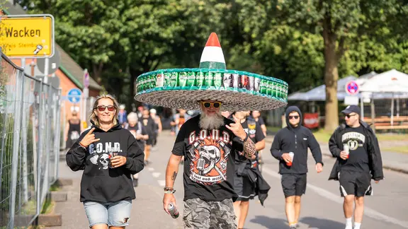 Metal-Fans auf der Hauptstraße in Wacken mit einem riesigen Hut aus Bierdosen. | NDR / Dominik Dührsen Metal-Fans auf der Hauptstraße in Wacken mit einem riesigen Hut aus Bierdosen.