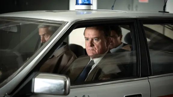 Harry Bowman (Silas Carson), Brian Boyce (Hugh Bonneville) und Edwyn Cooper (Dominic Cooper). Die Polizei entdeckt, dass die Erlöse des Raubs über ausländische Konten von Parry und Cooper gewaschen wurden. Keith Potts wird mit gewaschenem Geld an der Grenze zu Liechtenstein erwischt.
| WDR/All3Media International Die drei Polizisten im Auto sind auf der Jagt nach den Gälwäschern aus dem Goldraub