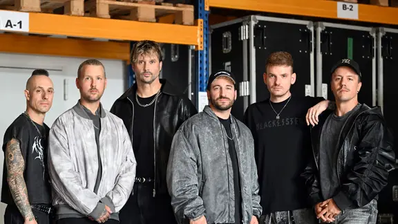 Das sind Electric Callboy: Frank Zummo, Daniel Haniß, Kevin Ratajczak, Nico Sallach, Pascal Schillo und Daniel Klossek (v.l.n.r.). | Federico Gambarini/dpa Die Band "Electric Callboy" aus Castrop-Rauxel steht in einer Halle.