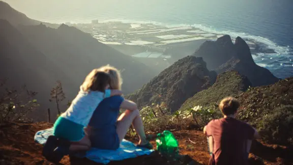 Szene aus dem Film "Everytime": Drei Personen sitzen auf einem Berg und blicken auf die Küste und das Meer | TheBarricades, PanamaFilm, Gregory Oke Szene aus dem Film "Everytime": Drei Personen sitzen auf einem Berg und blicken auf die Küste und das Meer