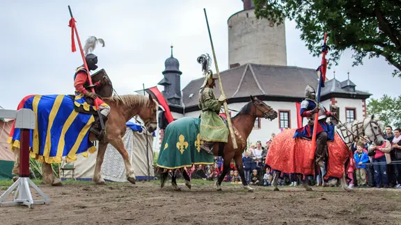 Beim Ritterfest auf Burg Posterstein reiten während des Ritterturniers die Ritter eine Ehrenrunde | picture alliance/Carsten Koall/dpa-Zentralbild/dpa Beim Ritterfest auf Burg Posterstein reiten während des Ritterturniers die Ritter eine Ehrenrunde
