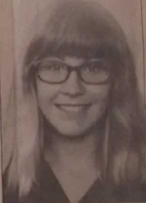A black and white photo of a smiling girl in glasses.