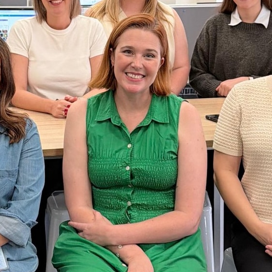 A group of people including a woman wearing a green dress sitting down in the front row