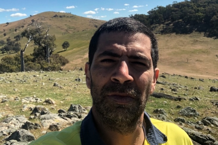 Man looking at camera with fields of rocks and trees in the background.