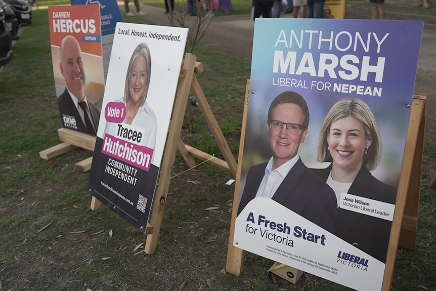 Wooden signs with people's names and photos of their faces stand on patchy grass.