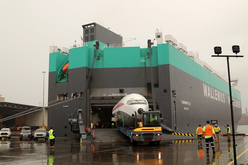 A wide shot of the plane bring taken off a large bulk carrier ship in a port.