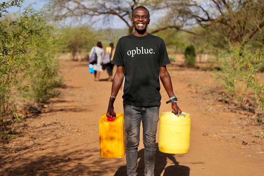 A man wearing an OpBlue t-shirt smiles and holds two plastic yellow water containers