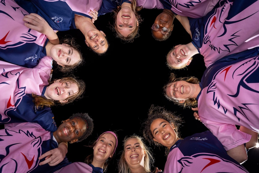 A ring of girls stand in a circle and look down.