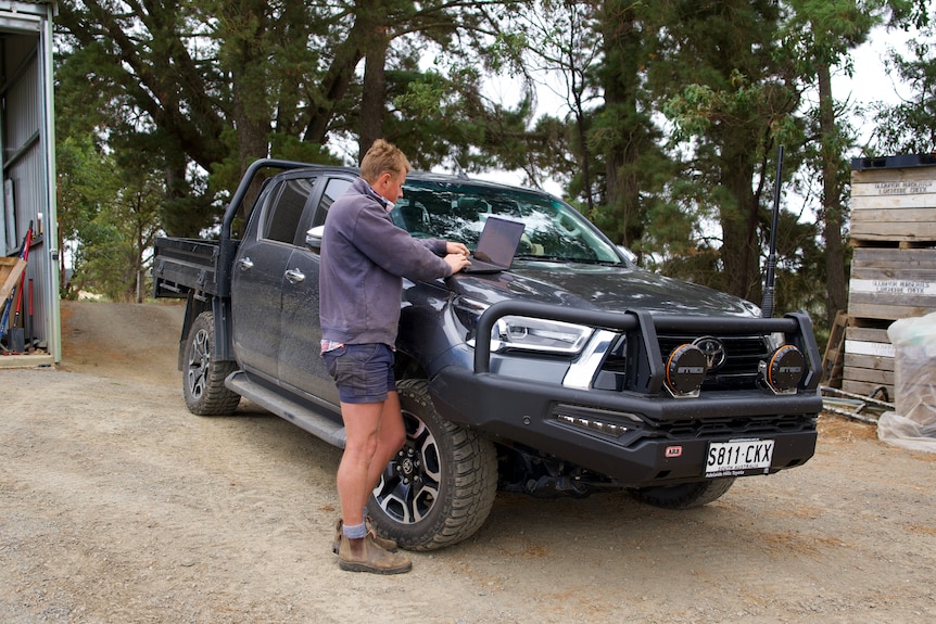 A man looks at his laptop on the bonnet of his ute.
