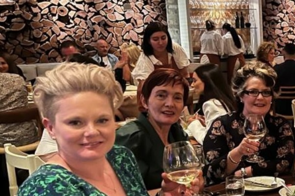 Roxanne, Gail and Angela sit in an expensive-looking restaurant, raising glasses and smiling.
