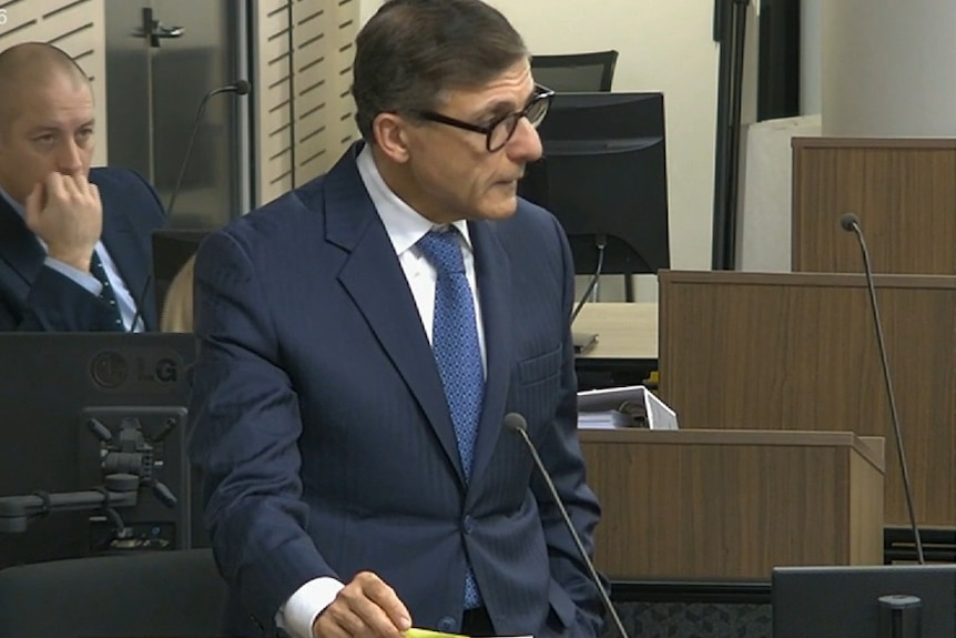 A man wearing thick black frame glasses standing at a podium.