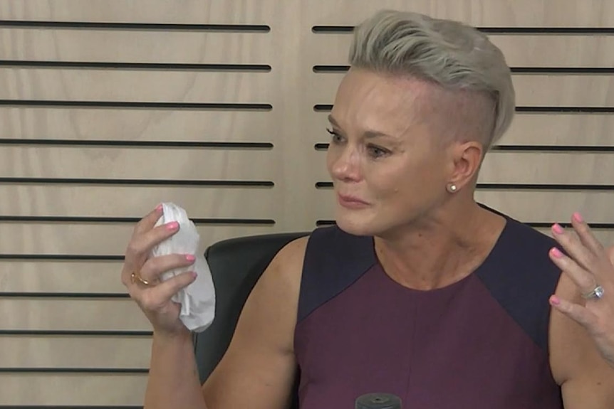 A woman with blonde hair in maroon and navy top holding a tissue