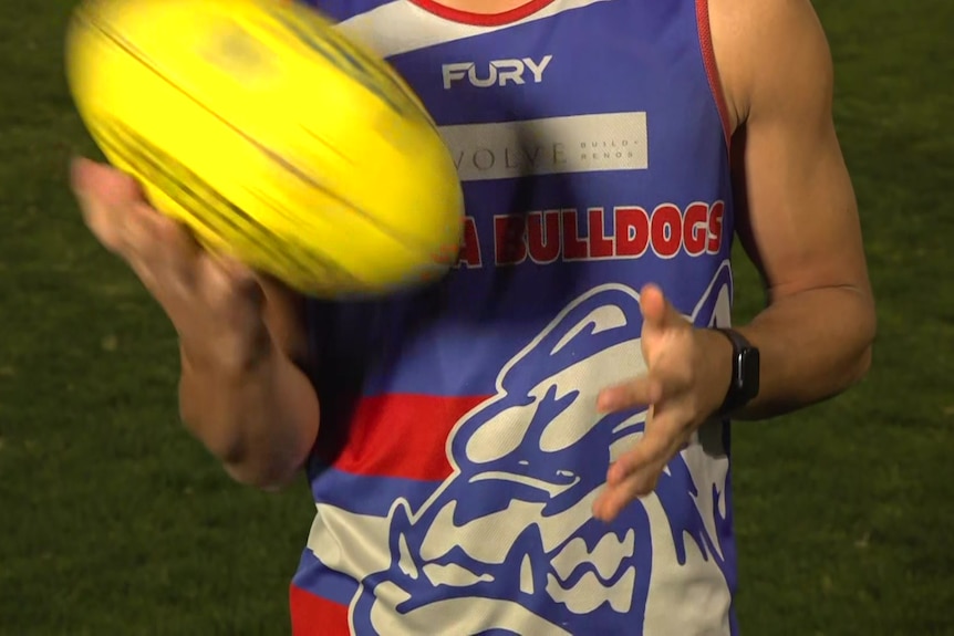 An unidentified young male in a red, white and blue jumper twirls a football.