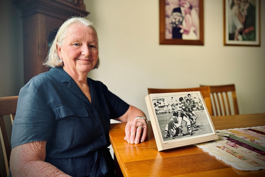 A woman wearing a navy dress sitting at a table with an old photograph.