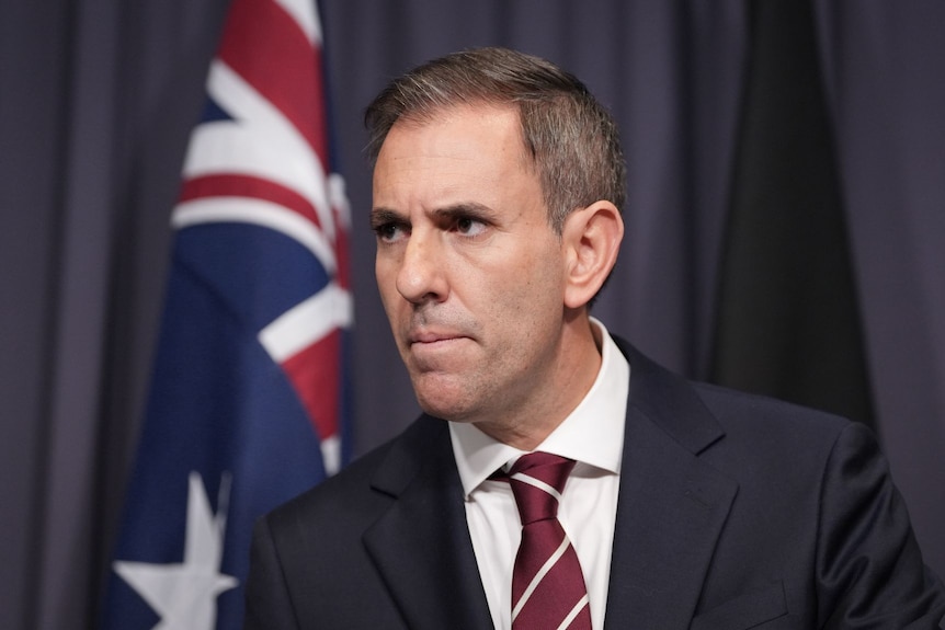 Treasurer Jim Chalmers in a navy suit and maroon tie, pressing his lips tightly.