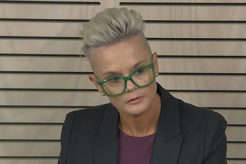 Woman with partly shaved andd blonde hair, black suit jackets and green glasses