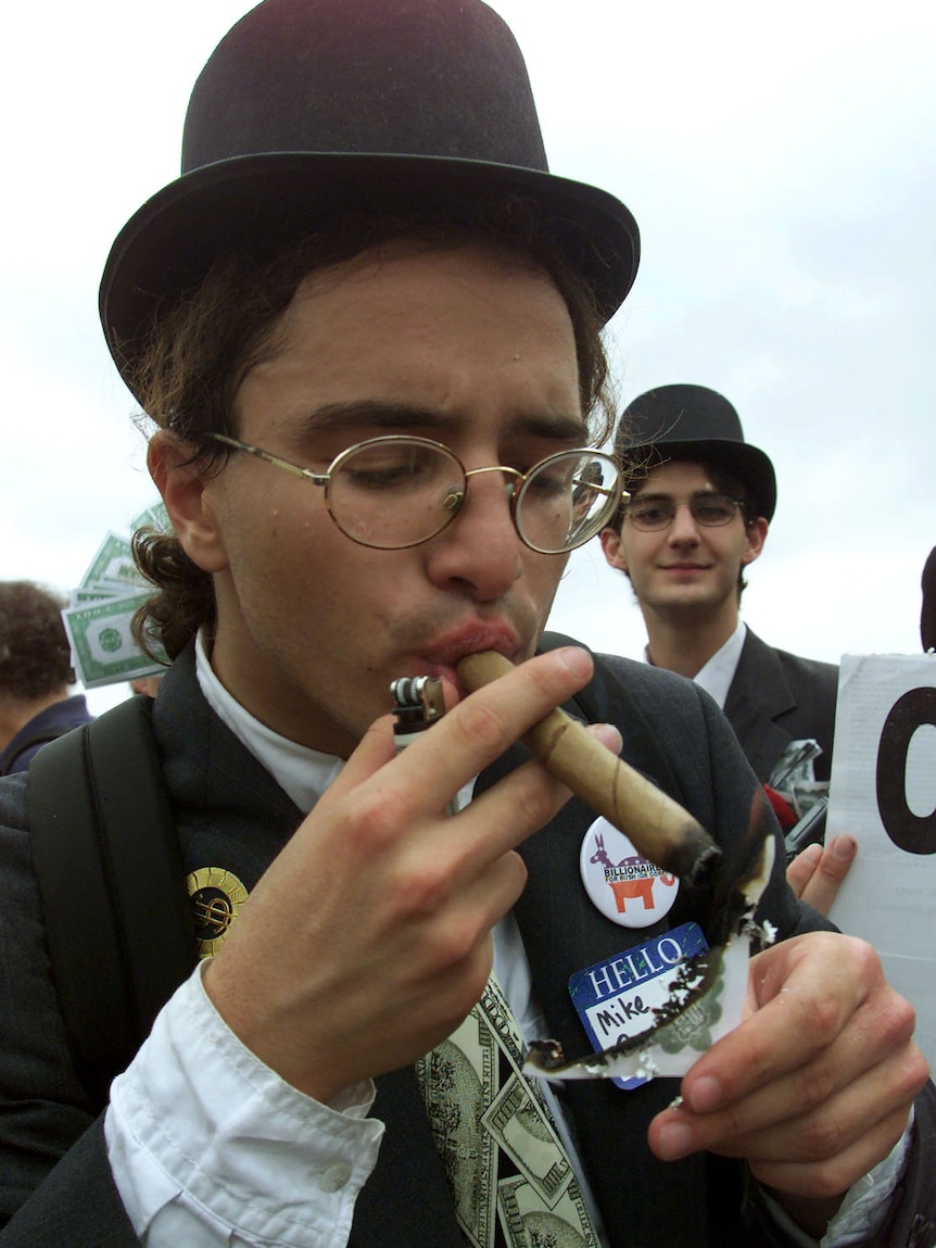 A man dressed up lights a cigar with a dollar note. 
