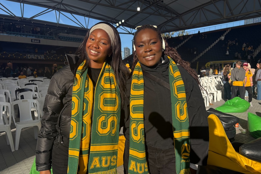 Two women smile while wearing green and gold scarves.