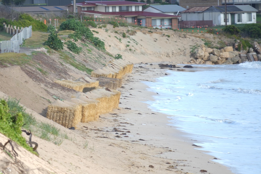 Hay bales on a beach with houses behind.