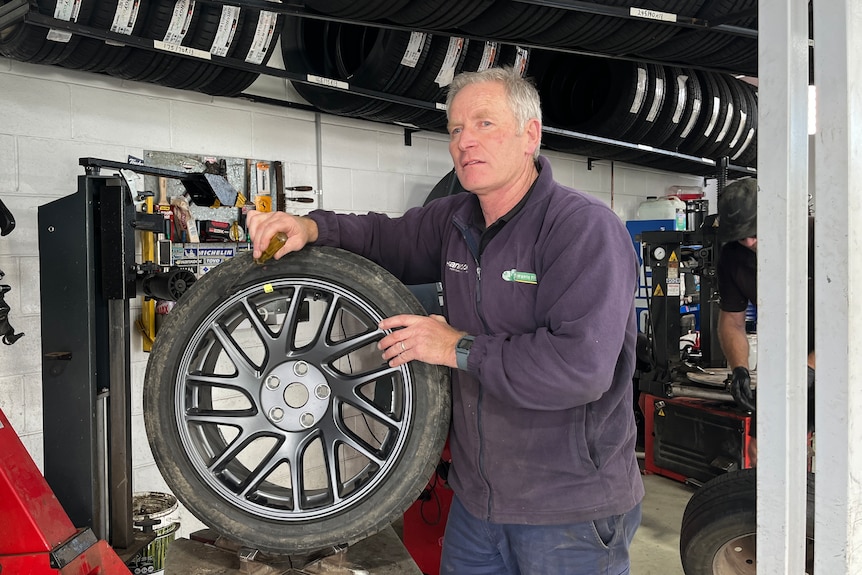 a man in a navy jumper stands in front of a tyre