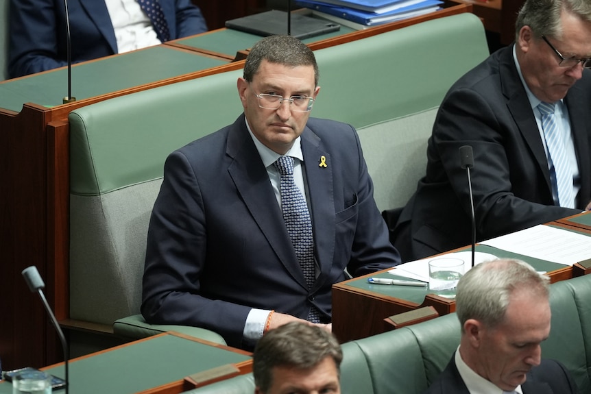A man in a blue suit wearing glasses sits in parliament