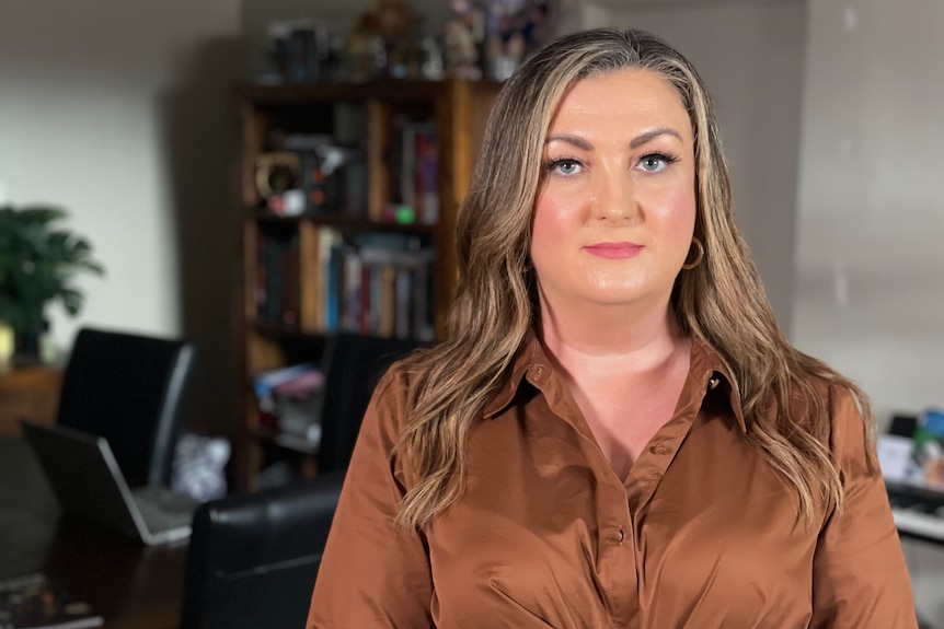 Woman in brown dress looks at camera in front of book case