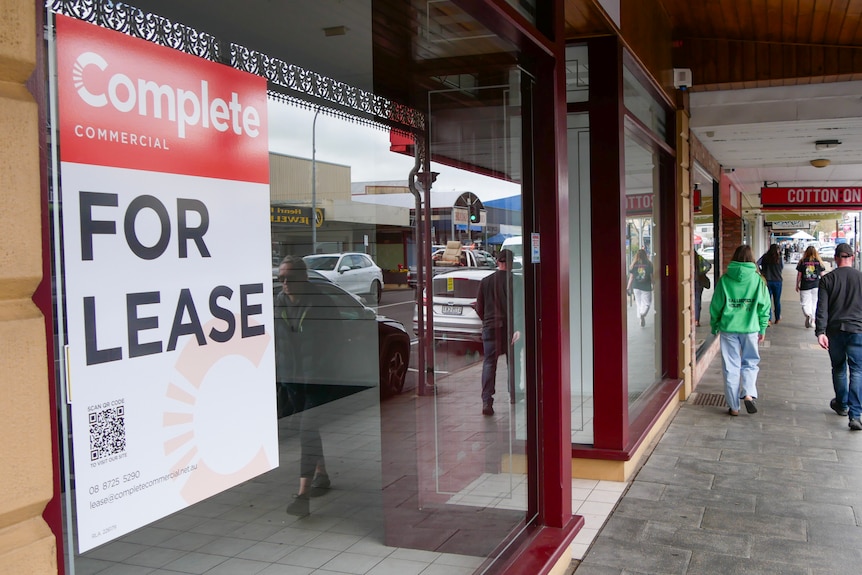 A for-lease sign on the left in an image showing the footpath of regional shopping street.