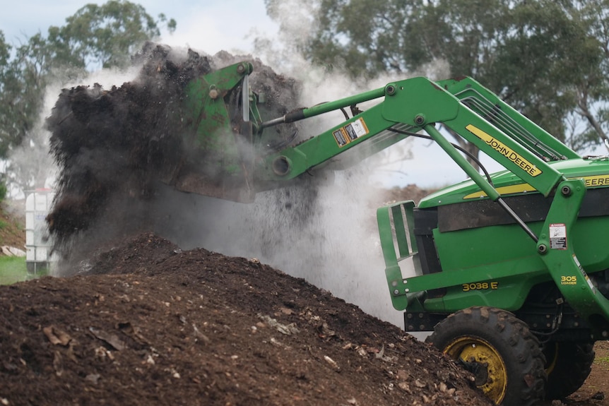 A tractor lifts compost up allowing a thick cloud of steam to escape