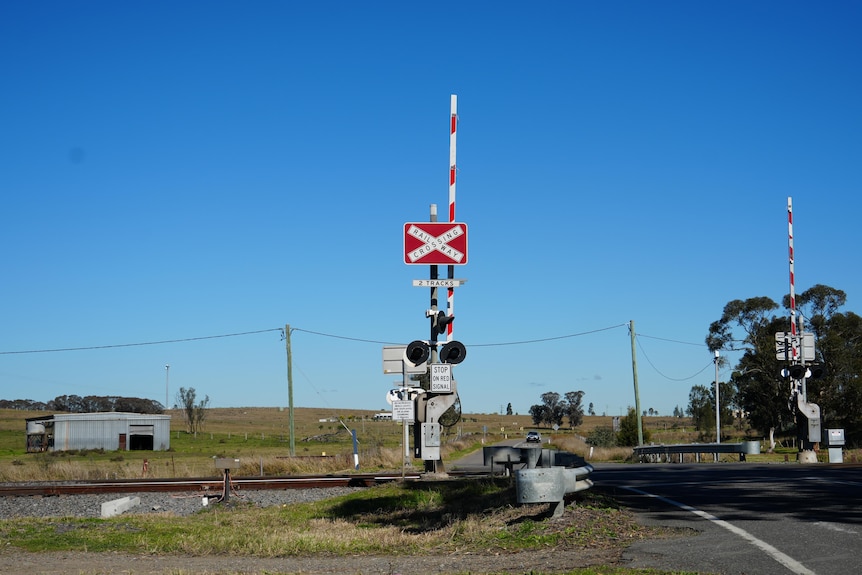 A picture of a level crossing taking from the road facing the train track.